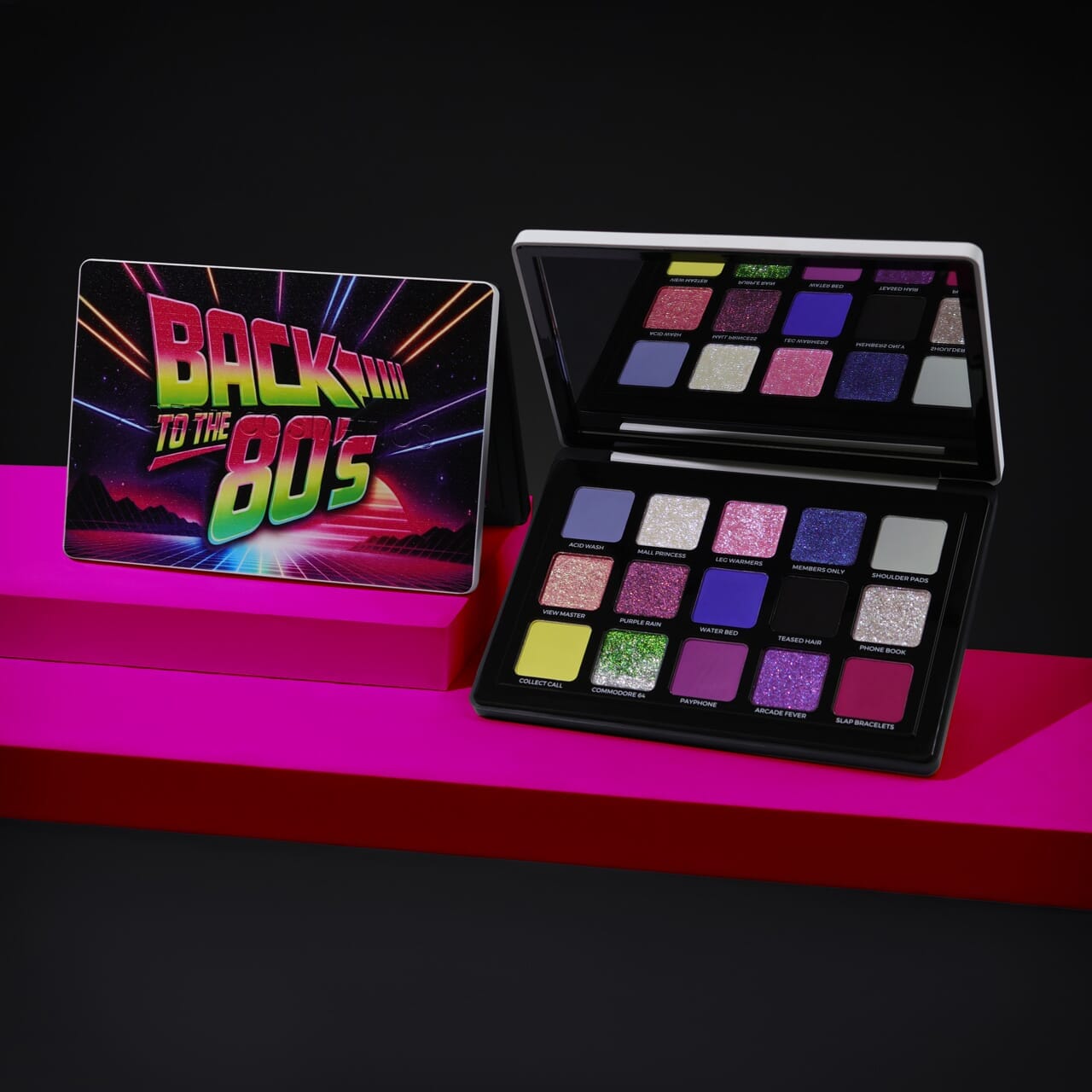 A 16-shade eyeshadow palette set displayed on a magenta platform against a black background. The closed palette on the left features a colorful retro 'Back to the 80's' design, while the open palette on the right displays various glitter and matte shades including pinks, purples, blues, greens, and yellows.
