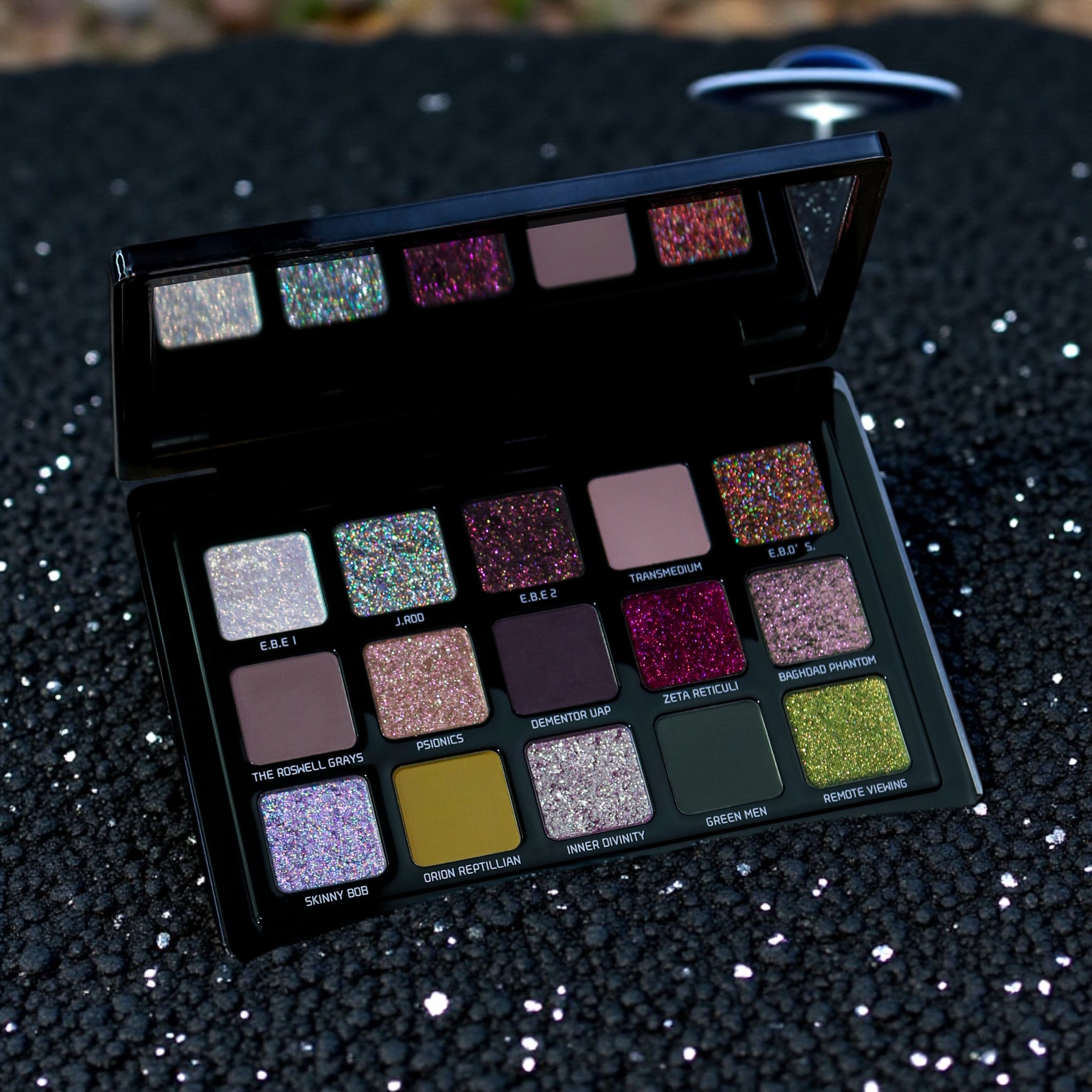 Makeup palette with various glittery eyeshadow shades on a black textured background