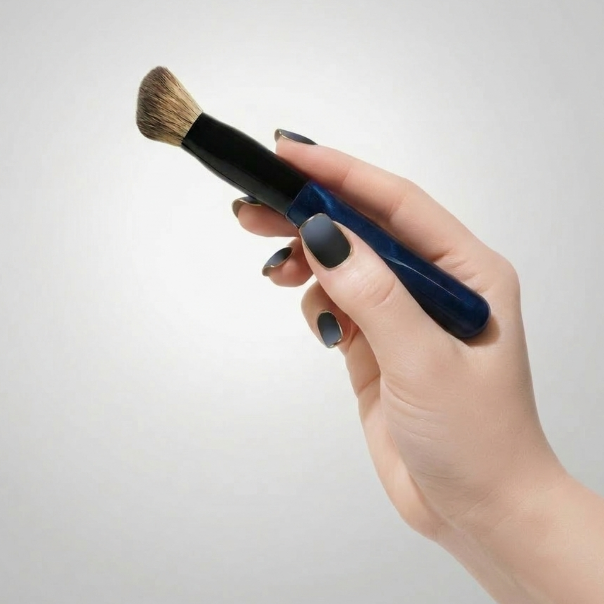 Hand holding a makeup brush with a blue handle against a light gray background