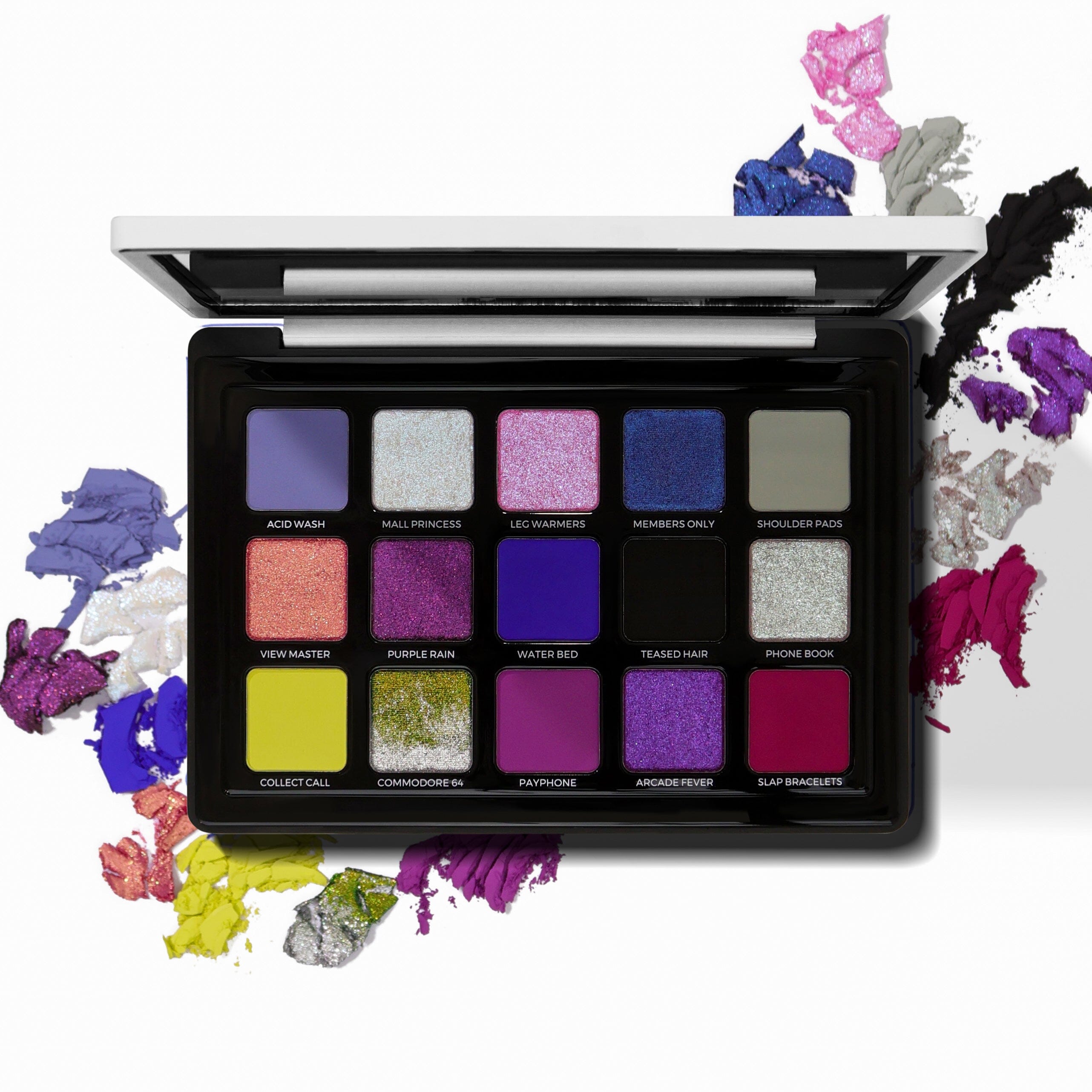 An open eyeshadow palette with 15 square pans in a black case, surrounded by colorful powder smears on a white background. The shades include various purples, pinks, blues, greens, yellows, and grays, with some labeled text visible on the pans.
