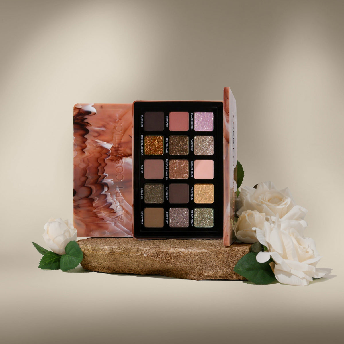 A 15-shade eyeshadow palette with a marbled terracotta and pink cover, displayed open on a rustic wooden block with white roses against a warm beige background.